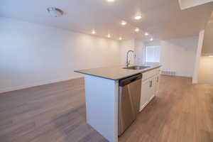 Kitchen with white cabinets, dishwasher, a center island with sink, recessed lighting, and light wood finished floors