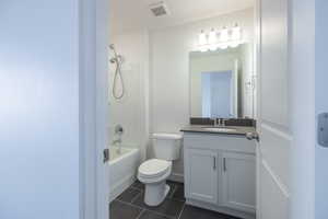 Bathroom with vanity, washtub / shower combination, and dark tile patterned floors