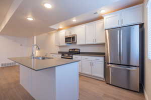 Kitchen with appliances with stainless steel finishes, white cabinets, light wood finished floors, recessed lighting, and a center island with sink