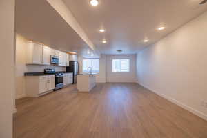 Kitchen with stainless steel appliances, open floor plan, white cabinets, light wood-style floors, and recessed lighting