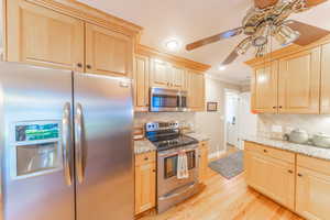 Kitchen featuring appliances with stainless steel finishes, light brown cabinets, light wood-type flooring, ceiling fan, and crown molding
