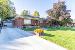 Ranch-style home featuring brick siding, a front lawn, an outbuilding, covered porch, and a detached garage