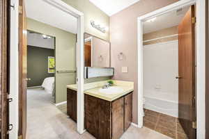 Ensuite bathroom featuring a textured wall, vanity, bathing tub / shower combination, light colored carpet, and light tile patterned flooring