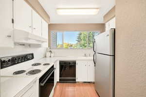 Kitchen with electric stove, a textured wall, freestanding refrigerator, light countertops, and dishwasher