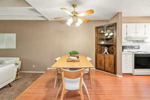 Dining space with a textured wall, ceiling fan, light wood finished floors, and a textured ceiling
