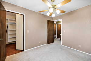 Unfurnished bedroom featuring a textured wall, carpet, a spacious closet, ceiling fan, and a textured ceiling