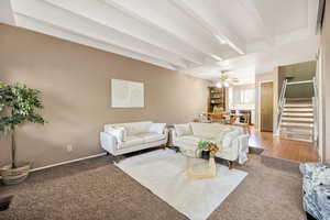 Carpeted living area with beam ceiling, stairs, a ceiling fan, wine cooler, and a textured wall