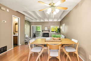 Dining space featuring light wood finished floors, a fireplace with raised hearth, a textured wall, beamed ceiling, and a textured ceiling