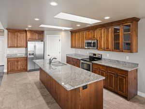 Kitchen with stainless steel appliances, brown cabinetry, recessed lighting, a skylight, and light stone countertops
