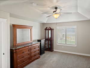 Bedroom with a raised ceiling, light carpet, and a ceiling fan