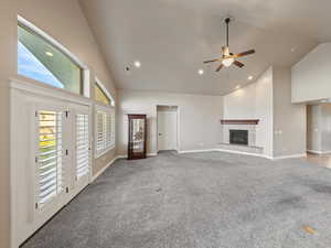 Unfurnished living room with high vaulted ceiling, carpet, recessed lighting, a fireplace with raised hearth, and a ceiling fan