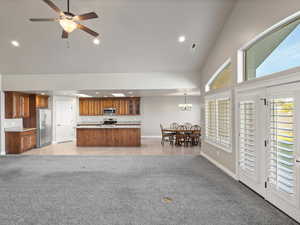 Kitchen featuring open floor plan, high vaulted ceiling, light carpet, brown cabinets, and appliances with stainless steel finishes