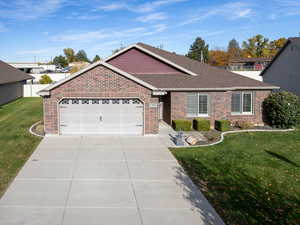 Single story home featuring a front lawn, an attached garage, driveway, a shingled roof, and brick siding