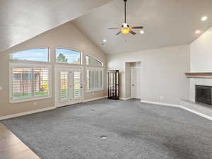 Unfurnished living room featuring a premium fireplace, light carpet, ceiling fan, high vaulted ceiling, and recessed lighting
