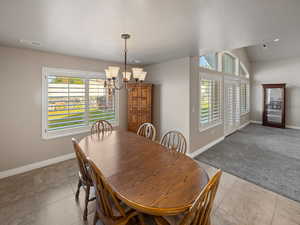 Carpeted dining space with plenty of natural light, a chandelier, tile patterned floors, a textured ceiling, and vaulted ceiling