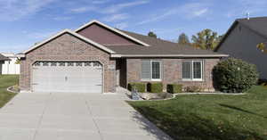 Single story home with a front yard, brick siding, concrete driveway, and an attached garage