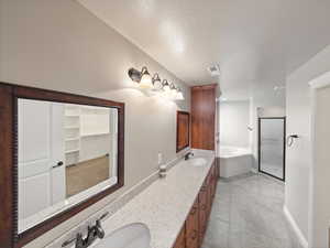 Bathroom featuring a bath, double vanity, a shower stall, light tile patterned floors, and a textured ceiling