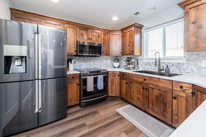 Kitchen featuring stainless steel appliances, tasteful backsplash, dark wood-type flooring, brown cabinetry, and recessed lighting