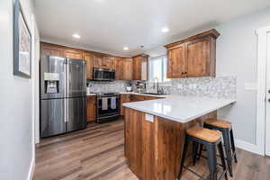 Kitchen with appliances with stainless steel finishes, a peninsula, a breakfast bar, dark wood-style flooring, and brown cabinetry