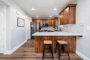 Kitchen with a breakfast bar, a peninsula, dark wood-style flooring, stainless steel appliances, and decorative backsplash