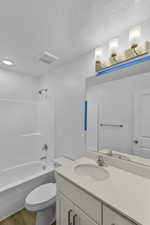 Bathroom featuring shower / bath combination, vanity, light wood-style floors, and a textured ceiling