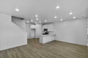 Kitchen with white cabinetry, light countertops, a peninsula, open floor plan, and dark wood-type flooring