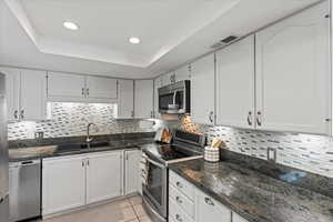 Kitchen featuring appliances with stainless steel finishes, white cabinetry, backsplash, dark stone countertops, and recessed lighting