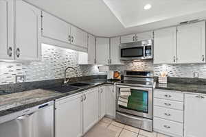 Kitchen with stainless steel appliances, white cabinets, light tile patterned flooring, and decorative backsplash