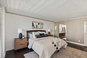 Bedroom with dark wood-style flooring, ornamental molding, a textured ceiling, and ensuite bath