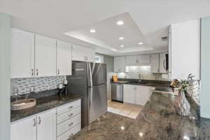 Kitchen with dark stone counters, stainless steel appliances, white cabinetry, decorative backsplash, and recessed lighting