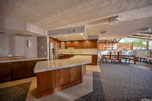 Kitchen with stainless steel appliances, a kitchen island, brown cabinets, a textured ceiling, and light stone countertops