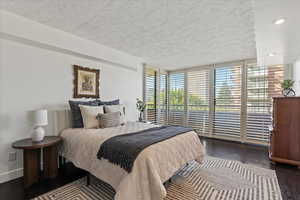 Bedroom with dark wood finished floors, access to outside, expansive windows, recessed lighting, and a textured ceiling