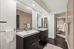 Full bathroom with two vanities, dark wood-style flooring, and recessed lighting