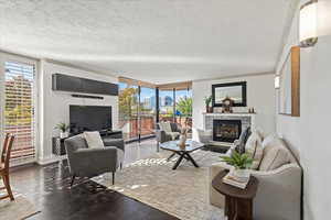 Living room with a wall of windows, a textured ceiling, a glass covered fireplace, crown molding, and dark wood-style floors