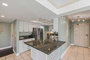Kitchen featuring white cabinetry, light tile patterned floors, stainless steel appliances, decorative backsplash, and ornamental molding