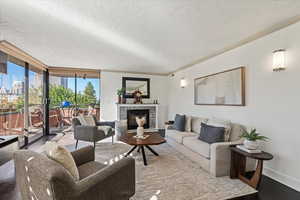 Living area featuring floor to ceiling windows, wood finished floors, a glass covered fireplace, a textured ceiling, and crown molding
