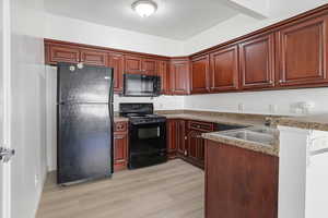 Kitchen with black appliances, light wood-style flooring, a peninsula, a textured ceiling, and dark countertops