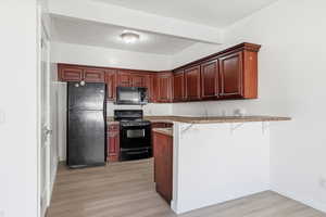 Kitchen featuring black appliances, a peninsula, a kitchen breakfast bar, and light wood-type flooring