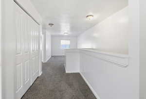 Hall featuring dark carpet, a textured ceiling, and an upstairs landing