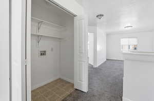 Laundry room featuring a textured ceiling, light colored carpet, light tile patterned flooring, and washer hookup
