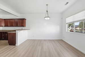 Kitchen with a peninsula, pendant lighting, a kitchen breakfast bar, light wood-style floors, and dark stone counters