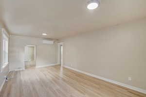 Empty room with light wood finished floors and a wall mounted AC