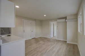 Kitchen with light wood finished floors, white cabinetry, recessed lighting, light stone countertops, and an AC wall unit