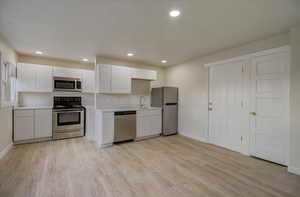 Kitchen featuring white cabinets, light countertops, appliances with stainless steel finishes, light wood-style flooring, and recessed lighting