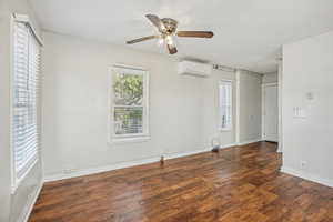 Unfurnished bedroom with multiple windows, dark wood-style flooring, and a ceiling fan