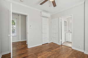 Unfurnished bedroom with crown molding, dark wood-type flooring, a wall mounted air conditioner, ceiling fan, and ensuite bathroom