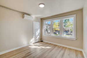 Unfurnished room with light wood-style floors and a wall mounted AC