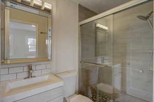 Bathroom featuring a stall shower, vanity, a textured wall, and tasteful backsplash