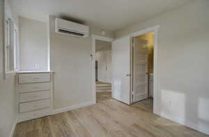 Unfurnished bedroom with light wood-style flooring, a wall mounted AC, and connected bathroom