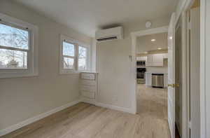 Empty room featuring light wood-style flooring and a wall mounted air conditioner
